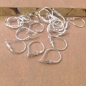 May include: A group of silver hoop earrings with a hinged closure. The earrings are arranged on a wooden surface.