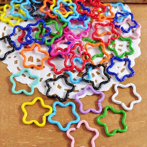 May include: A collection of colorful metal star-shaped jump rings. The rings are arranged on a white doily and are various sizes and colors, including red, blue, green, yellow, orange, purple, and black.