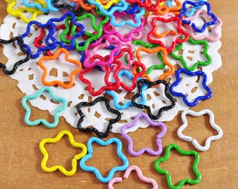 Könnte beinhalten: Eine Sammlung von bunten, sternförmigen Sprungringen aus Metall. Die Ringe sind auf einem weißen Doily angeordnet und haben verschiedene Größen und Farben, darunter Rot, Blau, Grün, Gelb, Orange, Lila und Schwarz.