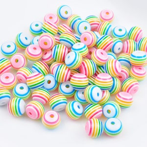 Puede incluir: Una colección de cuentas redondas de rayas de arcoíris de colores. Las cuentas son de plástico y tienen un acabado brillante.