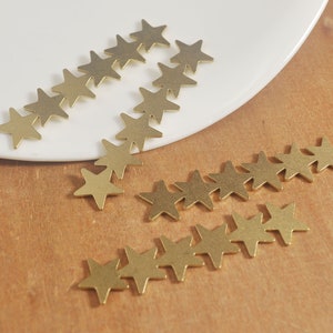 May include: A collection of gold-colored metal star shapes scattered on a white surface and a wooden surface.