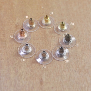 Peut inclure: Huit dos d'oreille de différentes couleurs, présentés sur une surface en bois. Chaque dos est sur un support en plastique transparent avec un numéro de 1 à 8.