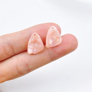 May include: Two pink triangle-shaped resin charms with a hole at the top. The charms have a marbled pattern.