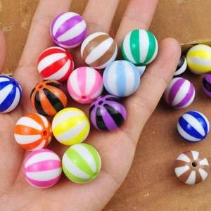 Puede incluir: Una colección de bolas de plástico rayadas de colores variados, incluyendo azul, verde, rojo, blanco, negro, marrón y morado.
