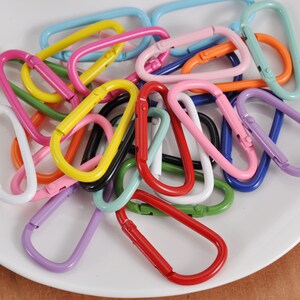 May include: A collection of colorful metal keychains in various shades of blue, green, red, pink, yellow, orange, and white. The keychains are shaped like a D-ring with a spring-loaded gate.