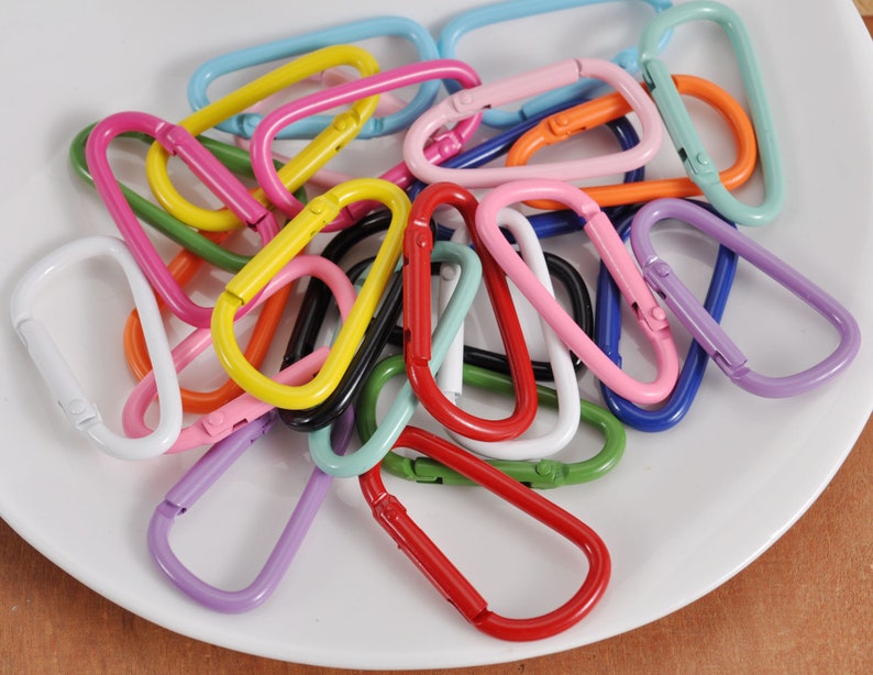 May include: A collection of colorful metal keychains in various shades of blue, green, red, pink, yellow, orange, and white. The keychains are shaped like a D-ring with a spring-loaded gate.