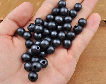 May include: A hand holding a pile of black wooden beads. The beads are round and have a smooth, matte finish.