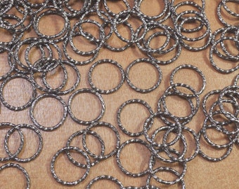 May include: A large pile of silver metal jump rings. The rings are all the same size and are arranged in a random pattern.