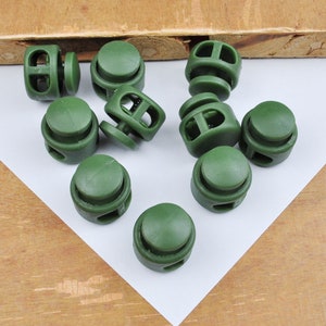 May include: A group of ten green plastic toggle clasps, also known as cord locks, for use in clothing, bags, or other projects.