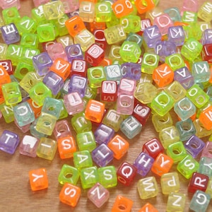 Könnte beinhalten: Ein großer Haufen bunter Plastikbuchstabenperlen. Die Perlen sind durchsichtig und haben weiße Buchstaben darauf. Die Buchstaben sind eine Mischung aus Groß- und Kleinbuchstaben.