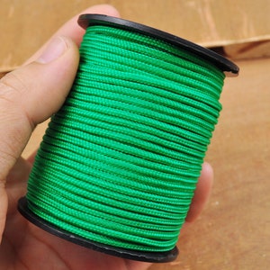 May include: A spool of bright green cord, tightly wound on a black plastic reel. The cord appears to be made of a synthetic material, with a slightly textured surface. The image is a close-up, highlighting the vibrant color and the cord's texture.