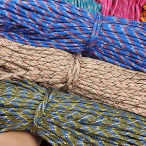 May include: Close-up of several bundles of colorful paracord rope. The ropes are in various colors, including blue, tan, green, pink, and orange. Each bundle is tied with a matching cord. The ropes have a diamond pattern.