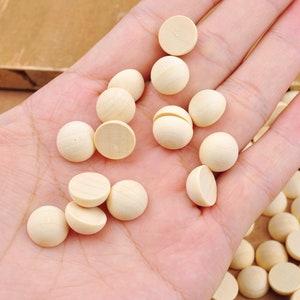May include: A hand holding a selection of small, unfinished wooden balls. The balls are smooth and round, and they are ideal for crafting projects.