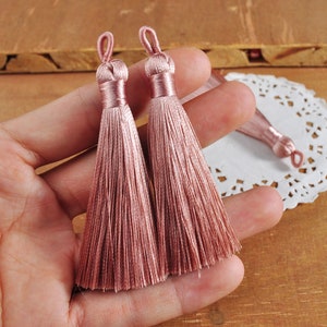 May include: Two dusty rose silk tassels with a loop at the top. The tassels are made of soft, fine threads and are approximately 2 inches long.