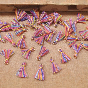Op de afbeelding: Een verzameling kleurrijke, meerkleurige kwastjes met gouden springringen. De kwastjes zijn gemaakt van garen en zijn ongeveer 2,5 cm lang.