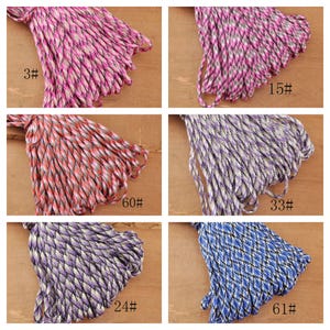 May include: A collection of colorful braided cords in various hues, including pink, purple, red, and blue. Each bundle is labeled with a number. The cords are tightly woven, creating a textured appearance. Ideal for crafting and DIY projects.