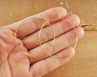 Puede incluir: Dos pendientes de aro dorados, que se muestran en una mano, son simples y elegantes.