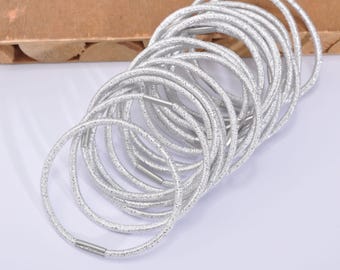 May include: A collection of silver elastic hair ties. Each tie is a thin, shimmering band with a metallic clasp. The ties are stacked together, creating a textured, layered effect. These hair accessories are suitable for various hairstyles.