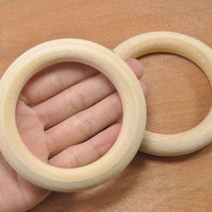 Puede incluir: Dos anillos de madera, uno más grande que el otro, se muestran en una imagen de primer plano. Los anillos son de color marrón claro y parecen estar hechos de madera sin terminar.