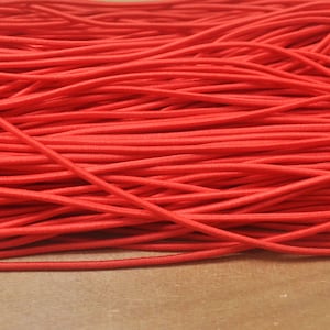 Può includere: Primo piano di una grande quantità di cordoncino elastico rosso. Il cordoncino è disposto in un mucchio, con i fili che si sovrappongono e si incrociano.