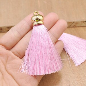 May include: Two pink silk tassels with gold metal caps. The tassels are approximately 5 cm long.