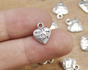 May include: Silver heart-shaped charms with the text "Made with Love" on them. The charms have a loop at the top for attaching to jewelry or other crafts.