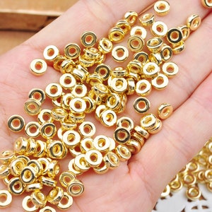 May include: A large pile of gold-colored metal beads, scattered on a hand. The beads are round and have a smooth, shiny finish.