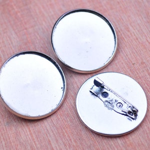 Puede incluir: Tres blancos redondos de metal plateados para hacer pines o broches personalizados. Los blancos tienen una superficie lisa y reflectante y están listos para ser decorados.