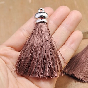 May include: Two brown tassel ornaments with silver metal caps. The tassels are made of soft, silky threads and are approximately 2 inches long.