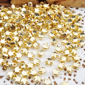 May include: A large pile of gold-colored crown-shaped beads. The beads are small and have a hole in the center for stringing.
