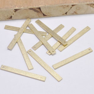 May include: A group of 12 gold-colored metal bar pendants with a hole at each end. The bars are arranged in a random pattern on a white surface.