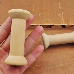 May include: Two wooden spools for thread or yarn. The spools are light brown and have a smooth, unfinished surface.