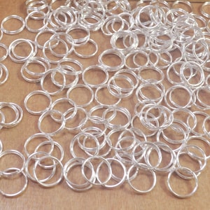 May include: A large quantity of silver jump rings, a type of metal ring used in jewelry making.