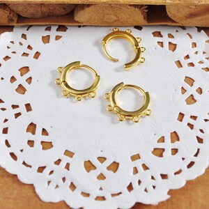 Peut inclure: Trois boucles d'oreilles en or avec cinq anneaux de saut sur chaque boucle. Les boucles d'oreilles sont sur une dentelle blanche.