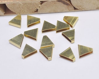 May include: A group of 15 gold-colored metal triangle shapes, scattered on a white surface. The triangles are about 1 inch in length and have a flat, smooth surface.