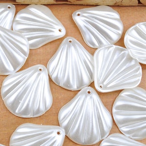 May include: A collection of white plastic shell-shaped embellishments with a pearlescent finish. The shells have a ridged texture and a hole at the top for stringing.