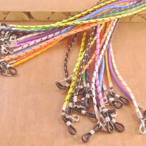 May include: A collection of colorful, patterned, and solid-colored eyeglass chains with metal clasps. The chains are made of a braided cord material.