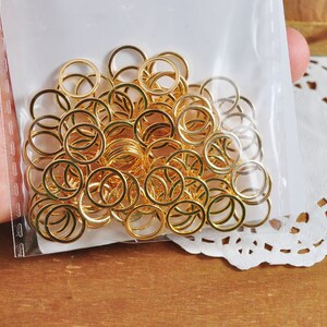 May include: A large quantity of gold jump rings in a clear plastic bag. The rings are all the same size and are arranged in a random pattern.