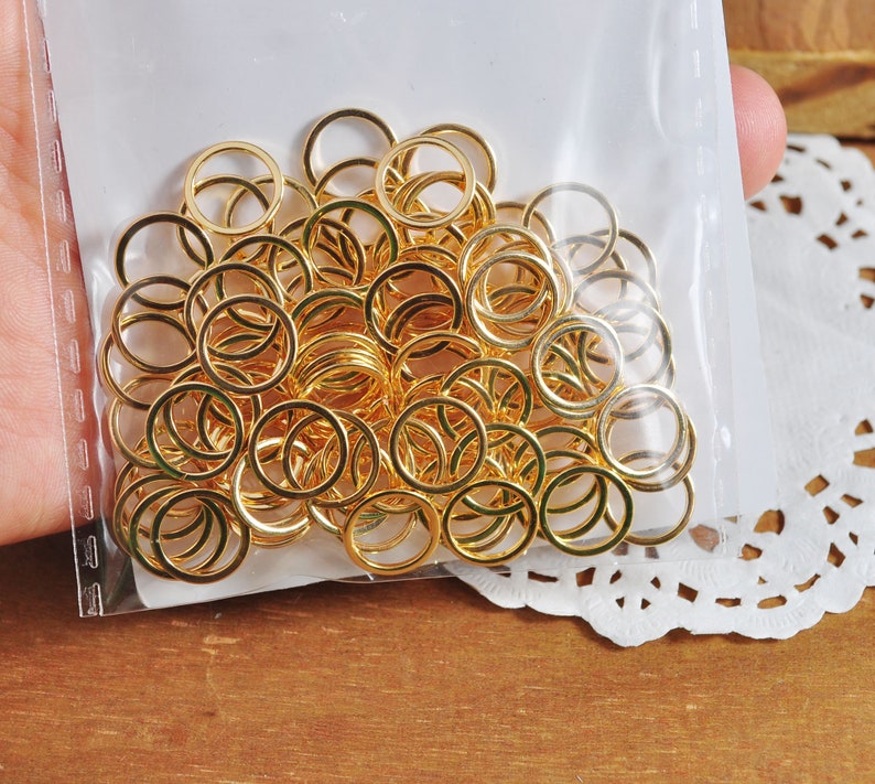May include: A large quantity of gold jump rings in a clear plastic bag. The rings are all the same size and are arranged in a random pattern.