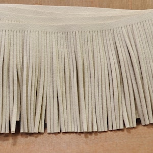 May include: A close-up of a beige suede fringe trim. The fringe is made of thin, soft strands of suede and is approximately 1 inch in length.