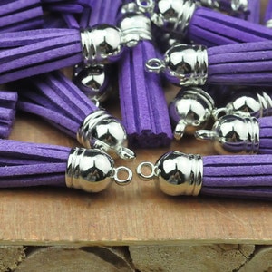 May include: A group of purple suede tassels with silver metal caps and loops. The tassels are arranged on a wooden surface.