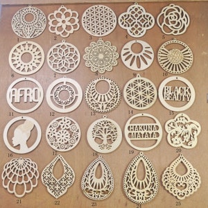 May include: Twenty-five wooden round and teardrop-shaped earring blanks with various laser-cut designs. The designs include geometric patterns, floral motifs, words like "Afro" and "Hakuna Matata", and a silhouette of a woman's head.