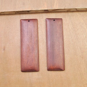 May include: Two rectangular wooden pendants with a hole at the top. The pendants are a reddish-brown color and have a smooth, polished finish.