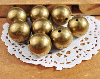 May include: A group of ten gold-colored round beads on a white doily. The beads are smooth and shiny.