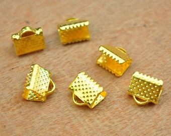 May include: Close-up of several small, gold-colored crimp end findings. These jewelry-making components have a rectangular shape with a textured surface and a crimped edge. Each piece has a small loop for attaching to other jewelry elements.