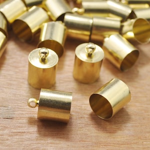 Pode incluir: Um grupo de tampas de metal dourado para cordões ou joias. As tampas são cilíndricas e têm um acabamento liso e brilhante.