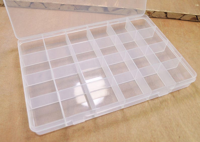 Puede incluir: Una caja de almacenamiento de pl&aacute;stico transparente con 24 compartimentos. La caja est&aacute; abierta y los compartimentos est&aacute;n vac&iacute;os.