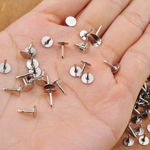 Könnte beinhalten: Nahaufnahme einer Hand, die einen Haufen silberner Metalltacker mit runden Köpfen und spitzen Spitzen hält. Die Tacker sind auf der Handfläche verstreut.