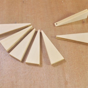 Op de afbeelding: Acht houten driehoeken met gaten aan de bovenkant, gerangschikt in een cirkel op een bruin oppervlak.