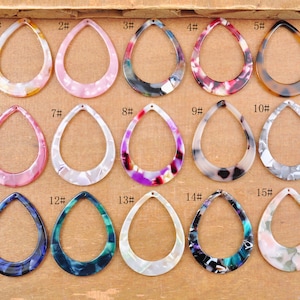May include: Fifteen different patterned plastic teardrop-shaped earring blanks with a hole at the top. The blanks are in various colors, including pink, black, white, purple, and green.